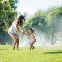Mother And Children playing Through Garden Sprinkler
